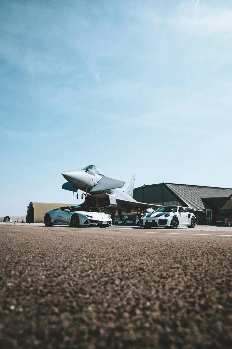 Exotic sports cars parked beside an aircraft on a runway
